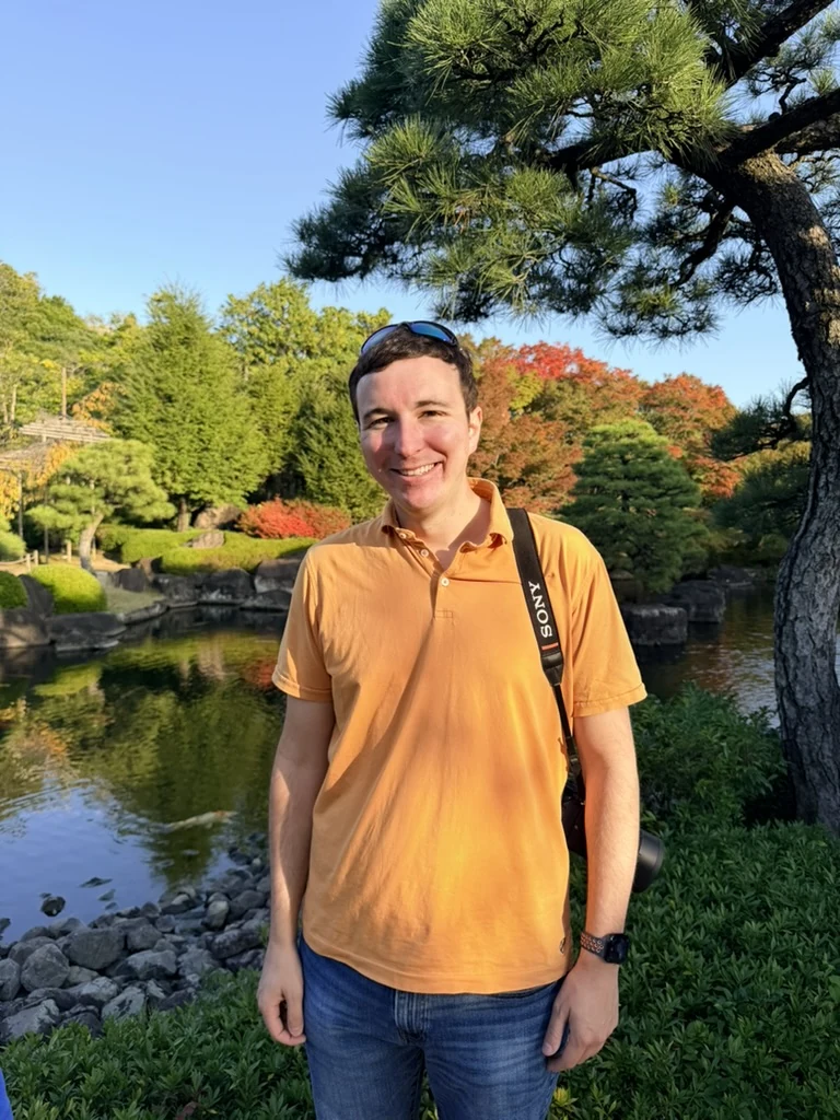 Addison Dent smiling beside a garden pond, with a camera over his shoulder