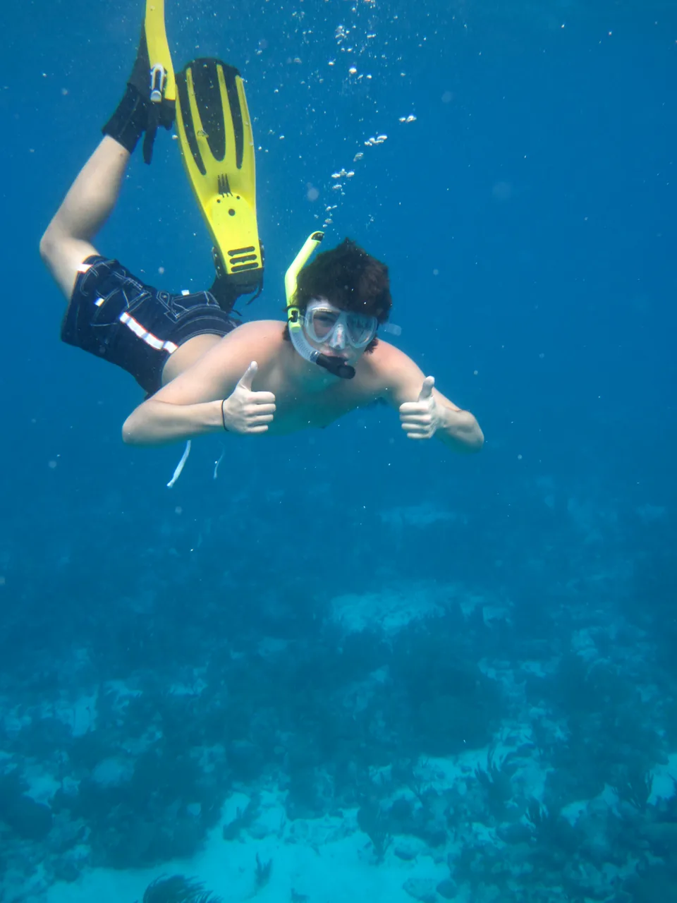 A snorkeler with yellow fins giving two thumbs up underwater
